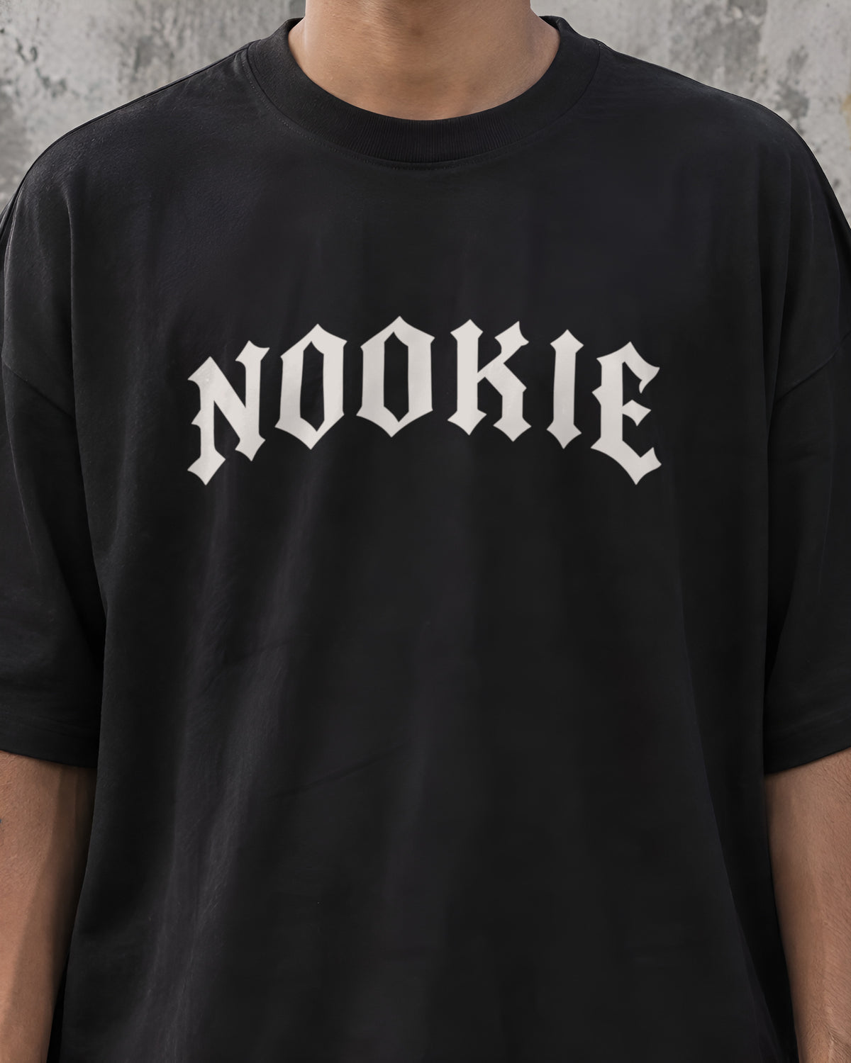 Close do logo NOOKIE em letra gótica branco osso, com 28 cm de largura, no peito da camiseta preta