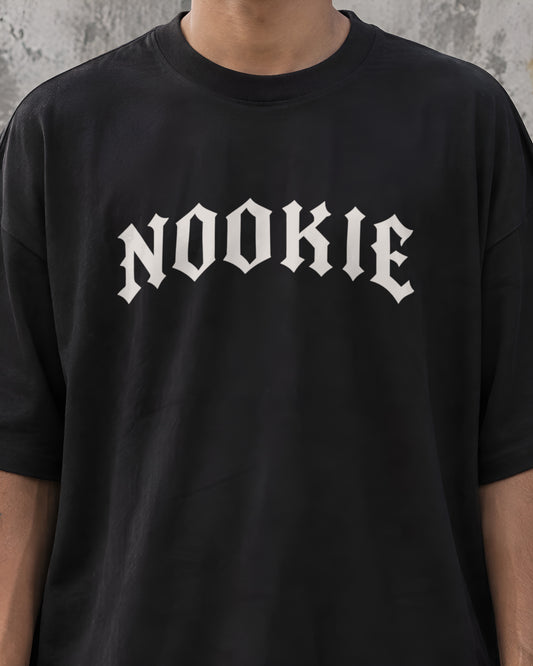 Close do logo NOOKIE em letra gótica branco osso, com 28 cm de largura, no peito da camiseta preta