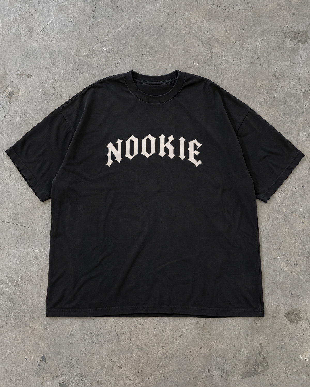 Camiseta oversized preta Nookie Manchete estendida no chão de concreto, frente com o logo NOOKIE no peito