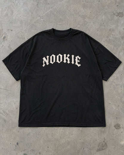 Camiseta oversized preta Nookie Manchete estendida no chão de concreto, frente com o logo NOOKIE no peito