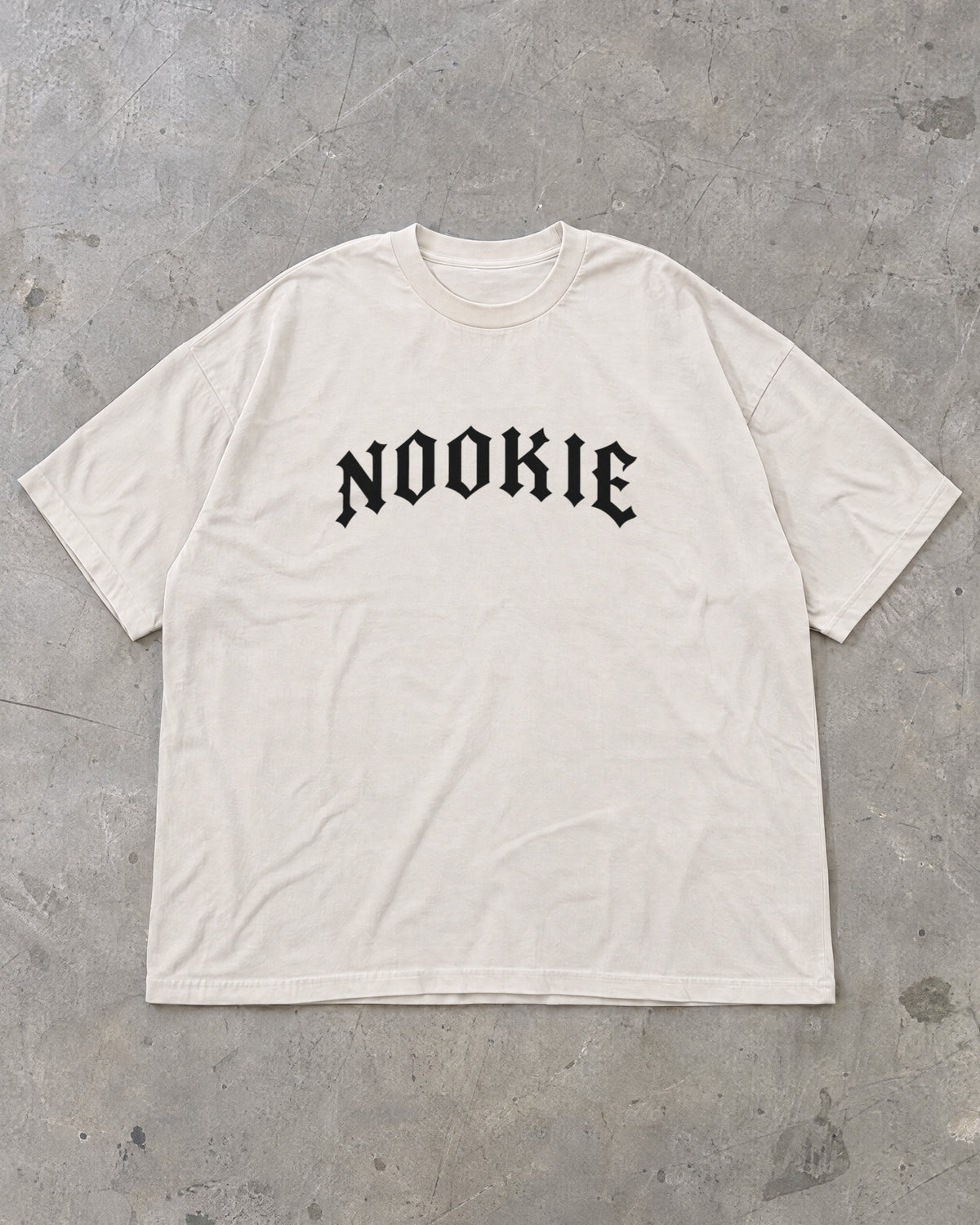 Camiseta oversized off-white Nookie Manchete estendida no chão de concreto, frente com o logo NOOKIE no peito